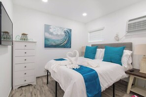 Een hotelkamer met een bed, een kapstok, een schilderij, een raam en een airconditioner.