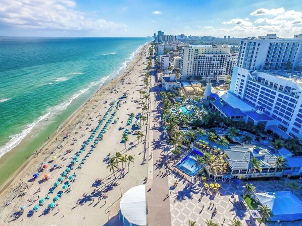 A beachside hotel with multiple levels, a pool area, and a beach with umbrellas. - Renovated studio w/ ocean views & boardwalk steps (Hollywood)