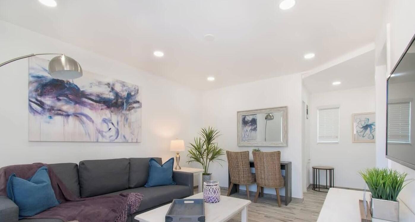 Un salon moderne avec un canapé, une table basse et un coin repas avec des chaises. On y trouve également des œuvres d’art accrochées au mur et un téléviseur à écran plat.