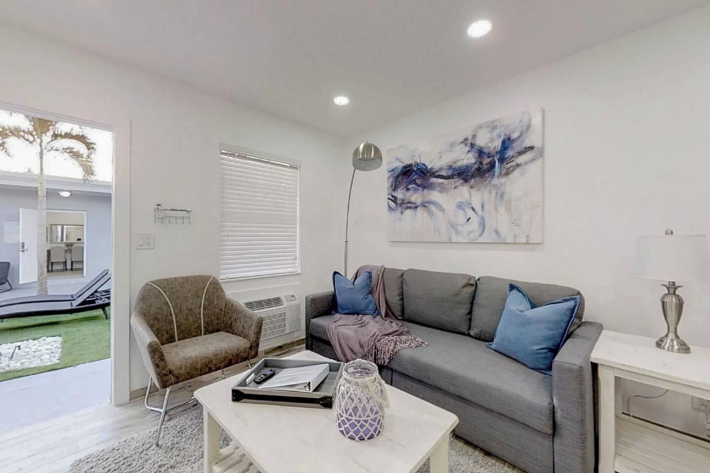 A modern living room with a grey sofa, a brown armchair, and a coffee table. There is a painting on the wall and a lamp on a side table.