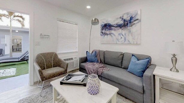 Ein modernes Wohnzimmer mit einem grauen Sofa, einem braunen Sessel und einem Couchtisch. An der Wand hängt ein Bild und auf einem Beistelltisch steht eine Lampe.