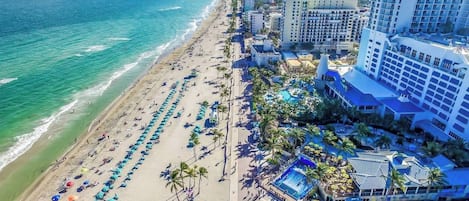 Un hotel frente a la playa con piscina, sombrillas y vistas al océano.