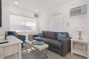 A modern living room with a grey sofa, a white coffee table, and a lamp on a side table. - Modern apartment w/beach steps & parking (Hollywood)