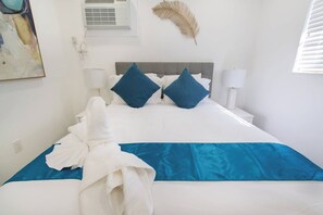 Une chambre d’hôtel comprenant un lit, des oreillers, une lampe de chevet, un climatiseur fixé au mur et un élément décoratif en plumes.
