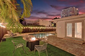A swimming pool area with a fire pit, lounge chairs, and a view of a building in the background. - Family-Friendly Beach House, Steps to Beach (Fort Lauderdale)