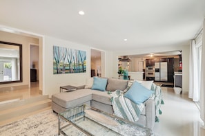 A modern living room with a sectional sofa, a glass coffee table, and a painting on the wall. - Family-Friendly Beach House, Steps to Beach (Fort Lauderdale)