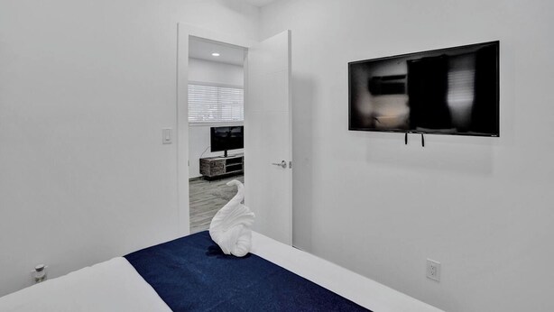 Una habitación minimalista con pared blanca, un televisor de pantalla plana montado y una puerta blanca que da a otra habitación.