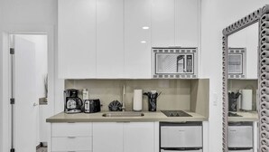 Una cocina moderna con armarios blancos, microondas integrado, cafetera y pileta.