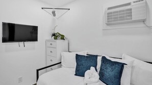 Habitación de hotel con cama, televisión, cómoda y unidad de aire acondicionado.