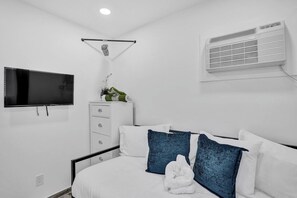 A hotel room with a bed, a TV, a dresser, and an air conditioning unit. - Spacious 2BR condo w/ beach access (Hollywood)