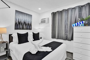 Ein Hotelzimmer mit einem Bett, einer weißen Kommode, einem Bild an der Wand und einem Fenster mit Vorhängen.