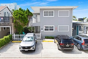 A two-story building with a grey facade, a white fence, and parked cars in front. - Bright 1BR aparthotel near beach w/ free parking (Hollywood)
