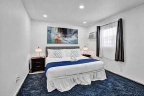 A hotel room with a large bed, two bedside tables, a wall-mounted air conditioning unit, and a window with curtains. - Bright 1BR aparthotel near beach w/ free parking (Hollywood)