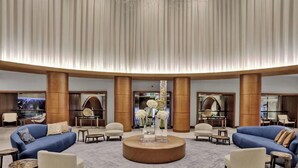 Eine geräumige Lobby mit einem runden Tisch in der Mitte, Sitzgelegenheiten und einer großen Kronleuchter.