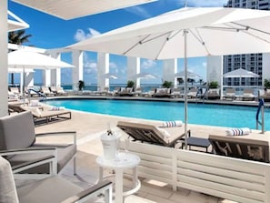 A poolside area with lounge chairs and umbrellas, a pool, and a view of the ocean. - 1BR condo w/ hot tub & gym access (Fort Lauderdale)