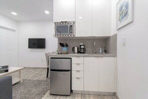 Een compacte keuken met een ingebouwde magnetron, een koelkast van roestvrij staal en een koffiezetapparaat.