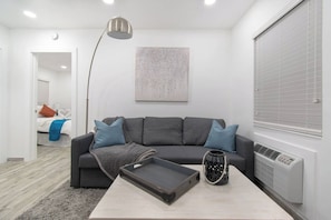 A modern living room with a grey sofa, a coffee table, and a floor lamp. - Modern apt w/queen bed & beach steps (Hollywood)
