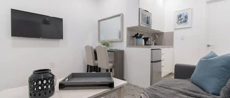 A modern, compact living space with a kitchenette, a flat-screen TV, a dining area, and a cozy seating area.