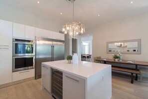 A modern kitchen with stainless steel appliances, a central island, and a dining area with a bench. - Modern villa close to beach w/ heated pool & grill (Hollywood)
