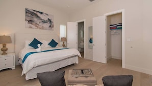 Ein Schlafzimmer mit Bett, Nachttischen, einer Lampe, einem Gemälde und einem begehbaren Kleiderschrank.