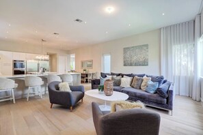 A modern living room with a grey sofa, a coffee table, and a dining area with white chairs. - Modern villa close to beach w/ heated pool & grill (Hollywood)