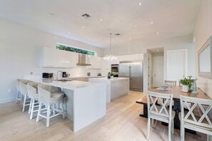 Een moderne keuken met een centraal eiland, barstoelen en een eettafel met stoelen.