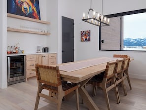 A modern kitchen with a wooden dining table and chairs, a built-in wine cooler, and artwork on the walls.