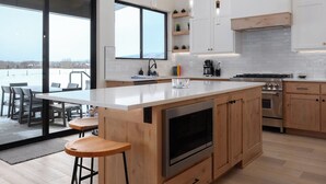Una cocina moderna con una isla grande, armarios de madera, electrodomésticos de acero inoxidable y vistas a través de la puerta de cristal.