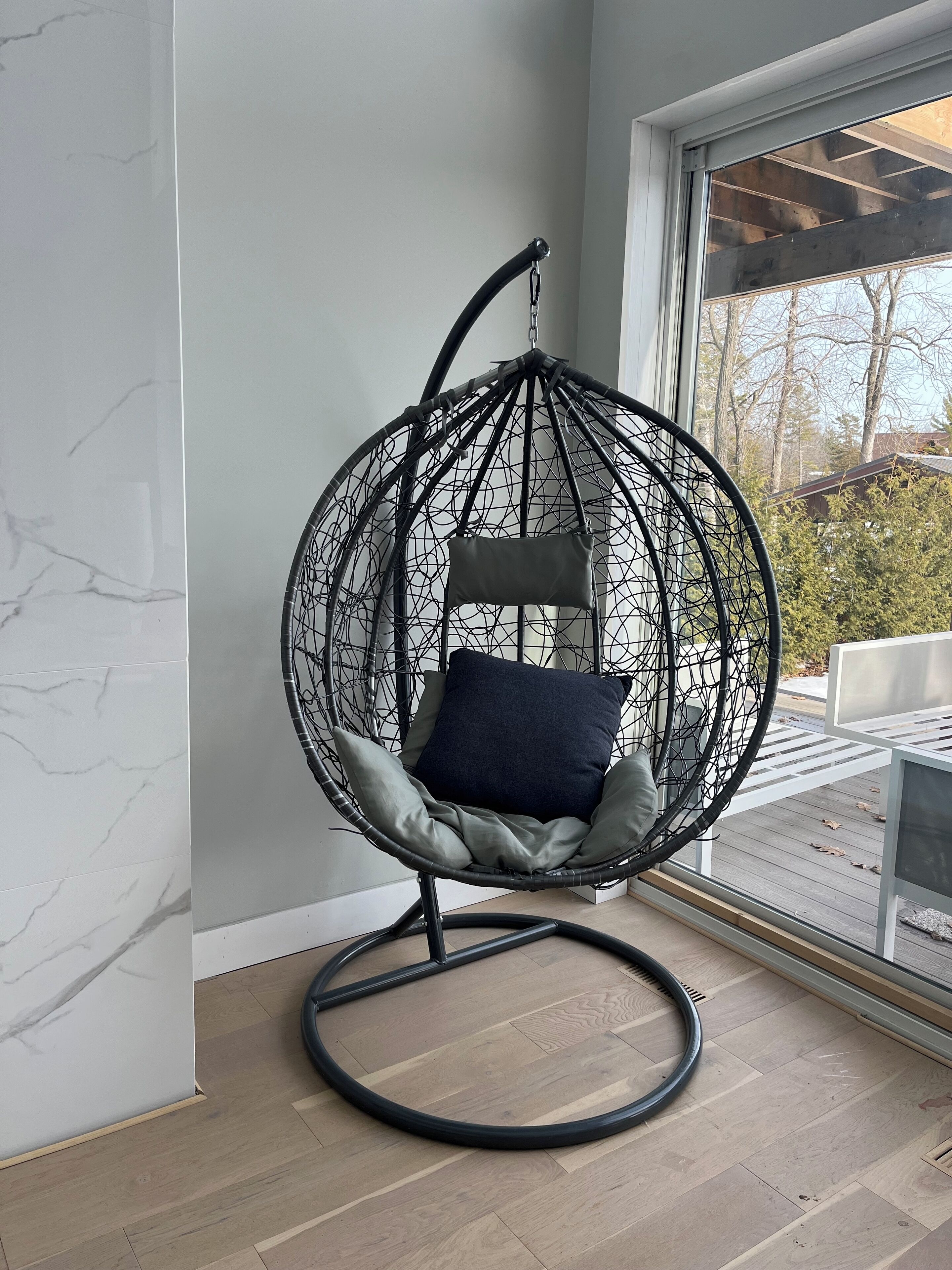 Une chambre moderne avec un fauteuil suspendu, une grande fenêtre et un plancher en bois.