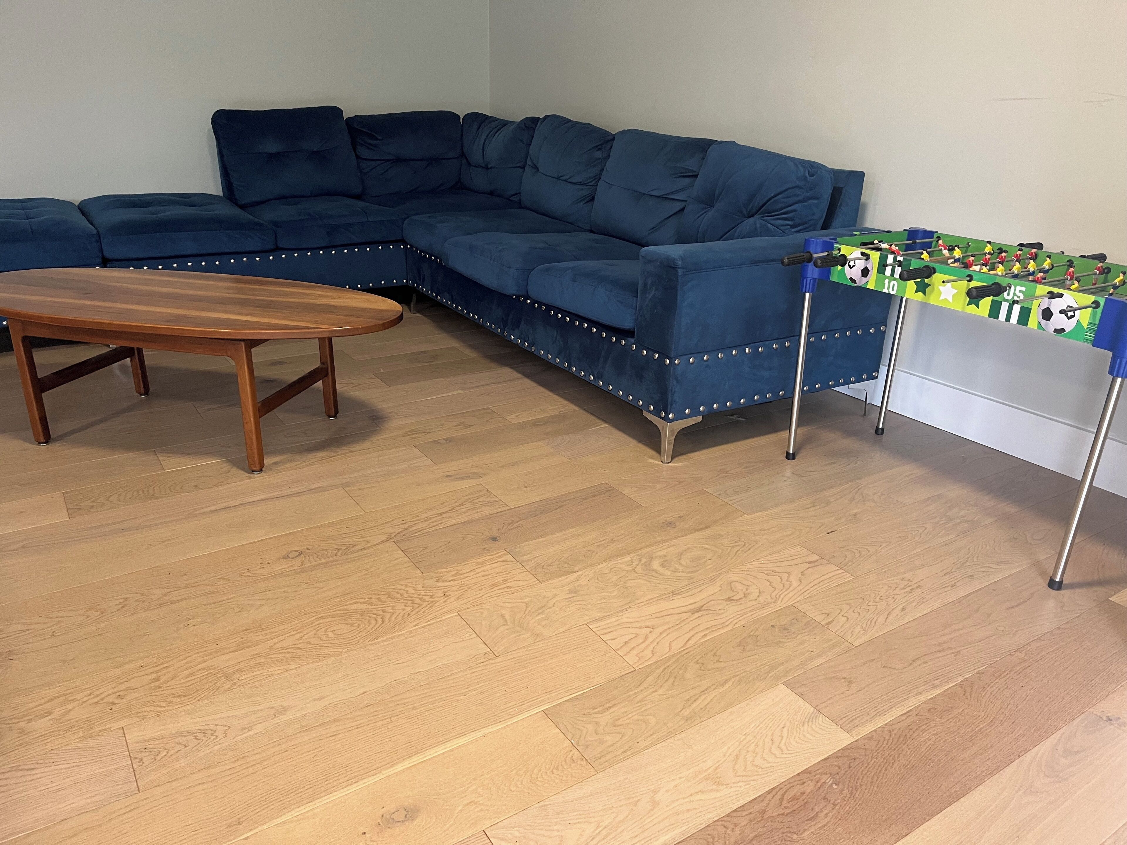 Une pièce avec un canapé d’angle bleu, une table basse en bois et une table de baby-foot.