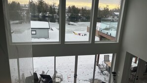 Una habitación con amplios ventanales que dan a un área exterior nevada, que incluye un muelle y un cobertizo pequeño.