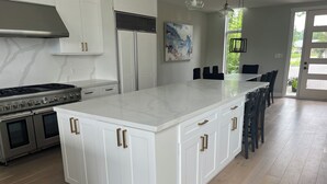 Una cocina con armarios blancos, una isla grande, electrodomésticos de acero inoxidable y vistas al exterior.