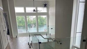Una habitación amplia con barandilla de vidrio, ventanas grandes y vista a un cuerpo de agua.