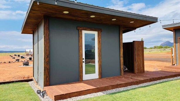 A modern, single-story building with a wooden deck and a door. - Unique Covered Wagon Glamping with Shared Sauna (Colorado City)