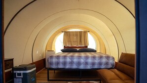 A cozy, circular room with a bed, a sofa, and a suitcase. - Unique Covered Wagon Glamping with Shared Sauna (Colorado City)