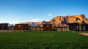 A grassy area with several wooden cabins and a mountain in the background. - Unique Covered Wagon Glamping with Shared Sauna (Colorado City)