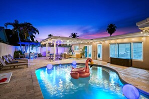 A swimming pool with a flamingo float, lounge chairs, and a covered patio area. - Spacious home w/pool, fire pit & grill (Lighthouse Point)