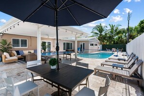An outdoor pool area with a table and chairs, lounge chairs, and a covered seating area. - Spacious home w/pool, fire pit & grill (Lighthouse Point)