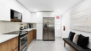 A modern kitchen with white cabinetry, stainless steel appliances, and a marble backsplash. - Spacious home w/pool, fire pit & grill (Lighthouse Point)
