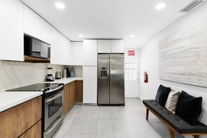 A modern kitchen with white cabinetry, stainless steel appliances, and a marble backsplash. - Spacious home w/pool, fire pit & grill (Lighthouse Point)