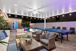 An outdoor pool area with a ping pong table, lounge chairs, and a ceiling fan. - Spacious home w/pool, fire pit & grill (Lighthouse Point)