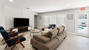 A modern living room with a flat-screen TV, a sofa, a coffee table, and a TV stand. - Spacious home w/pool, fire pit & grill (Lighthouse Point)