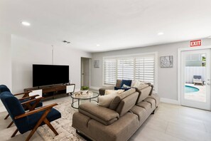 A modern living room with a flat-screen TV, a sofa, a coffee table, and a TV stand. - Spacious home w/pool, fire pit & grill (Lighthouse Point)