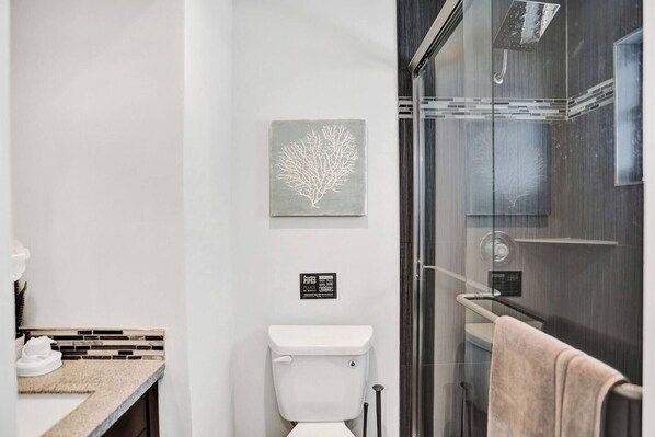 Et moderne badeværelse med brusekabine i glas, toilet og håndvask med flisebeklædt bagvæg.