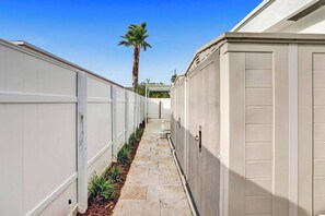 A narrow pathway flanked by storage units, leading to a palm tree. - Spacious home w/pool, fire pit & grill (Lighthouse Point)