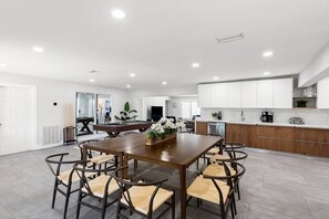 A modern kitchen with white cabinets, a wooden dining table, and chairs. - Spacious home w/pool, fire pit & grill (Lighthouse Point)