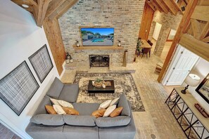 A spacious living area with a gray sofa, a fireplace, and a television mounted on a brick wall. - Family villa w/ heated pool, gameroom & fire pit (Davie)
