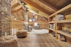 A loft-style room with exposed wooden beams, a brick wall, two armchairs, a round rug, and a bookshelf with books. - Family villa w/ heated pool, gameroom & fire pit (Davie)