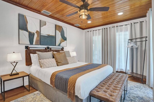 A bedroom with a bed, bedside tables, a ceiling fan, artwork, curtains, and a bench. - Family villa w/ heated pool, gameroom & fire pit (Davie)