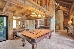 A pool table in a room with wooden beams, a bar area, and a stone wall. - Family villa w/ heated pool, gameroom & fire pit (Davie)